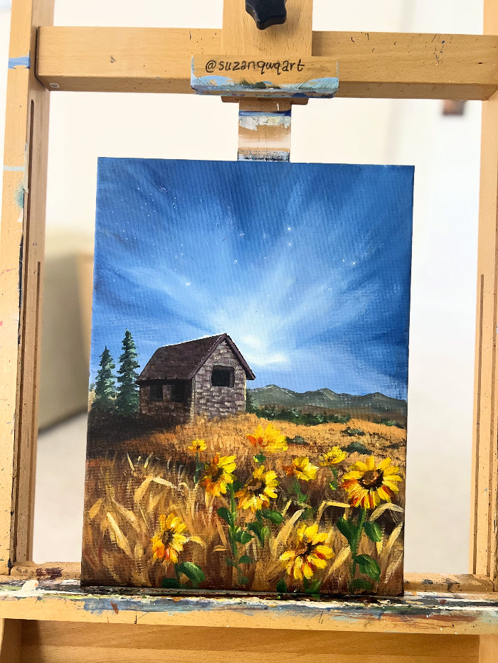 Painting of a sunflower field with a cabin on an easel.