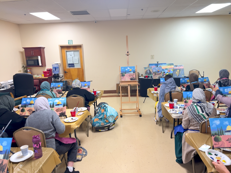 Group of people in a classroom setting with art supplies and easels.